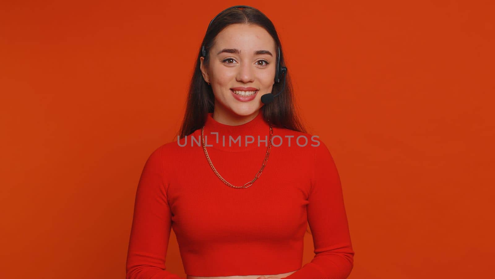 Smiling pretty woman wearing headset, freelance worker, call center or support service operator helpline, having talk with client or colleague, communication support. Young girl on red background