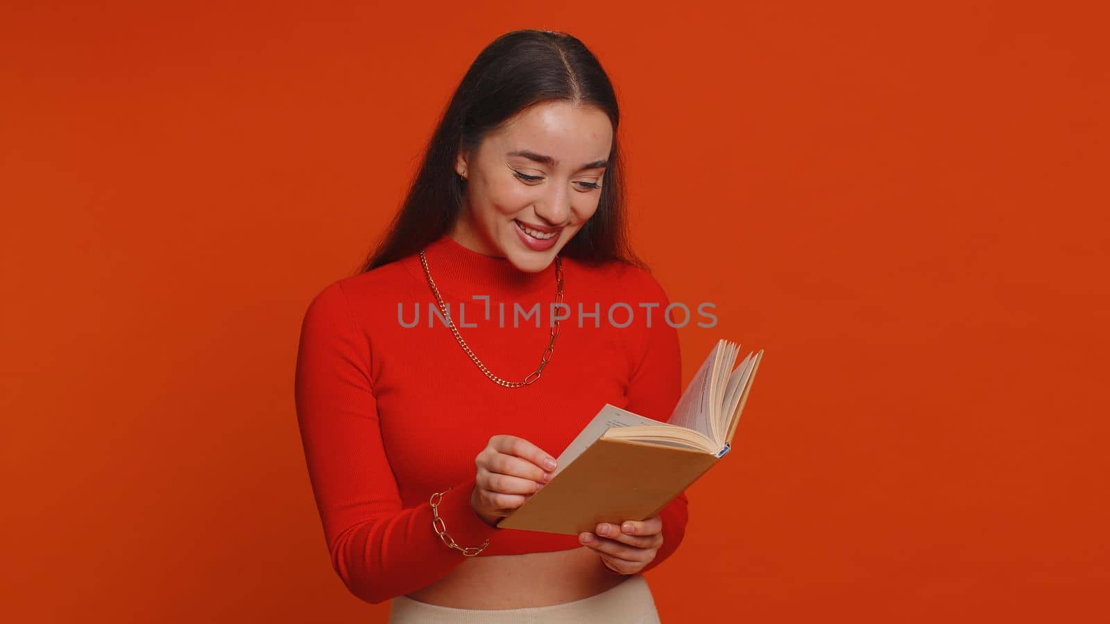 Happy pretty woman reading funny interesting fairytale story book, leisure hobby, knowledge wisdom, education, learning study, wow inspiration. Young adult girl isolated alone on red studio background