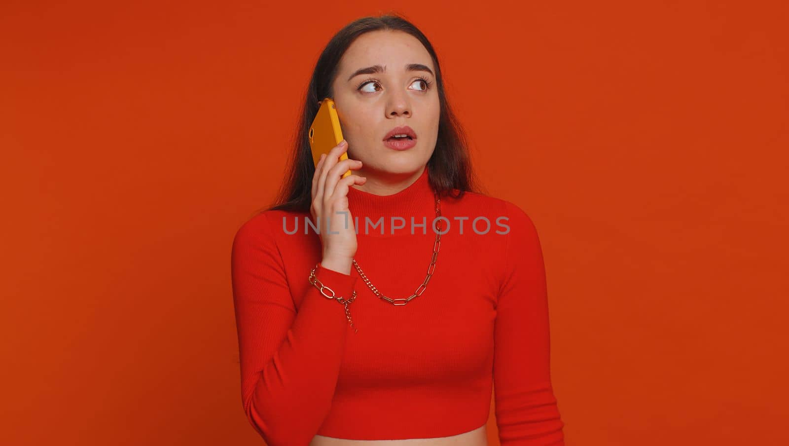 Lovely woman tired sleepy freelancer talking on mobile phone with friend, making online conversation. Disinterested sad young girl having annoyed boring talk on smartphone on red studio background