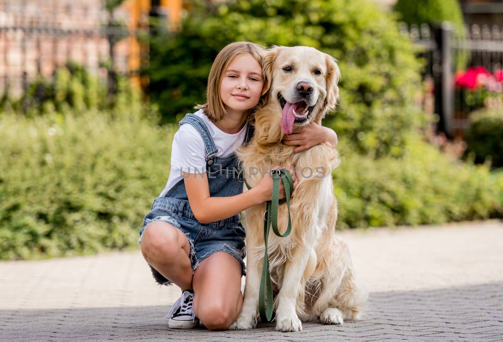 Preteen girl petting golden retriever dog at street. Female child kid with purebred dog labrador sits on ground.