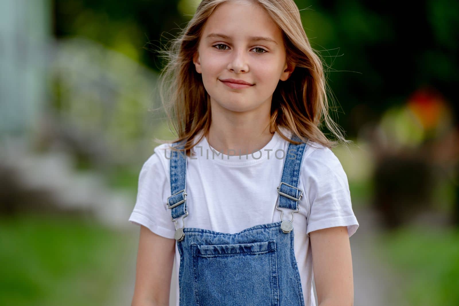 Beautiful preteen girl in city in summertime closeup portrait. Pretty female kid looking at camera in sunny day with blurred background