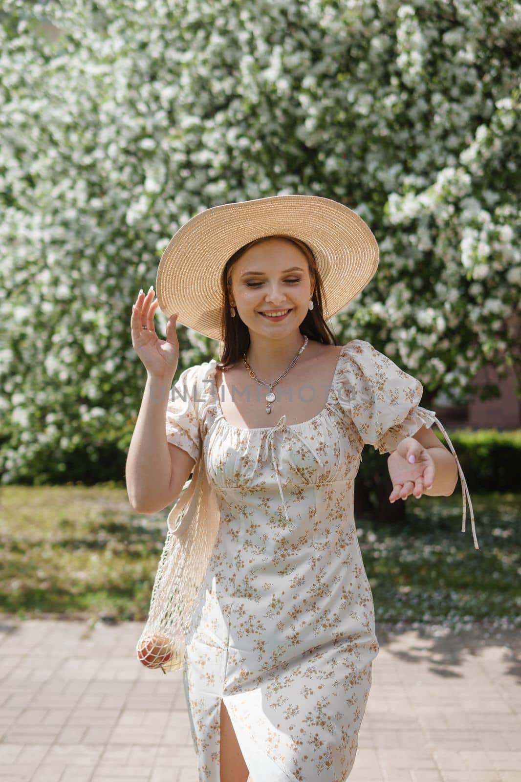 An attractive long-haired woman walks in the spring in the park of blooming apple trees. Spring portrait of a woman