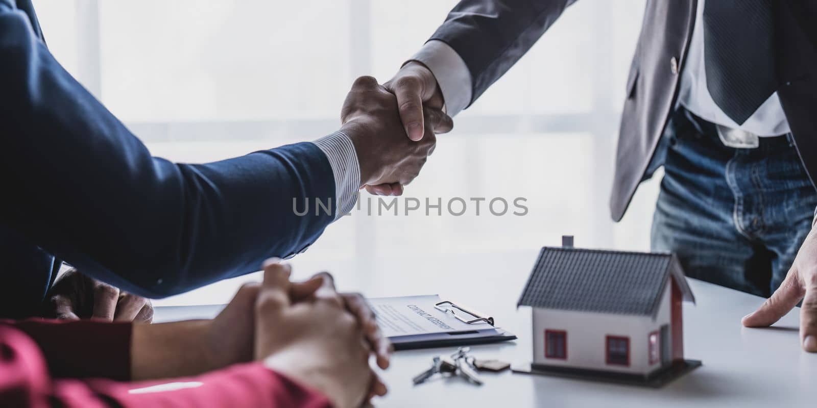 Good deal buy new house Cheerful young man bonding to his wife while shaking hand to man sitting in front of him at office