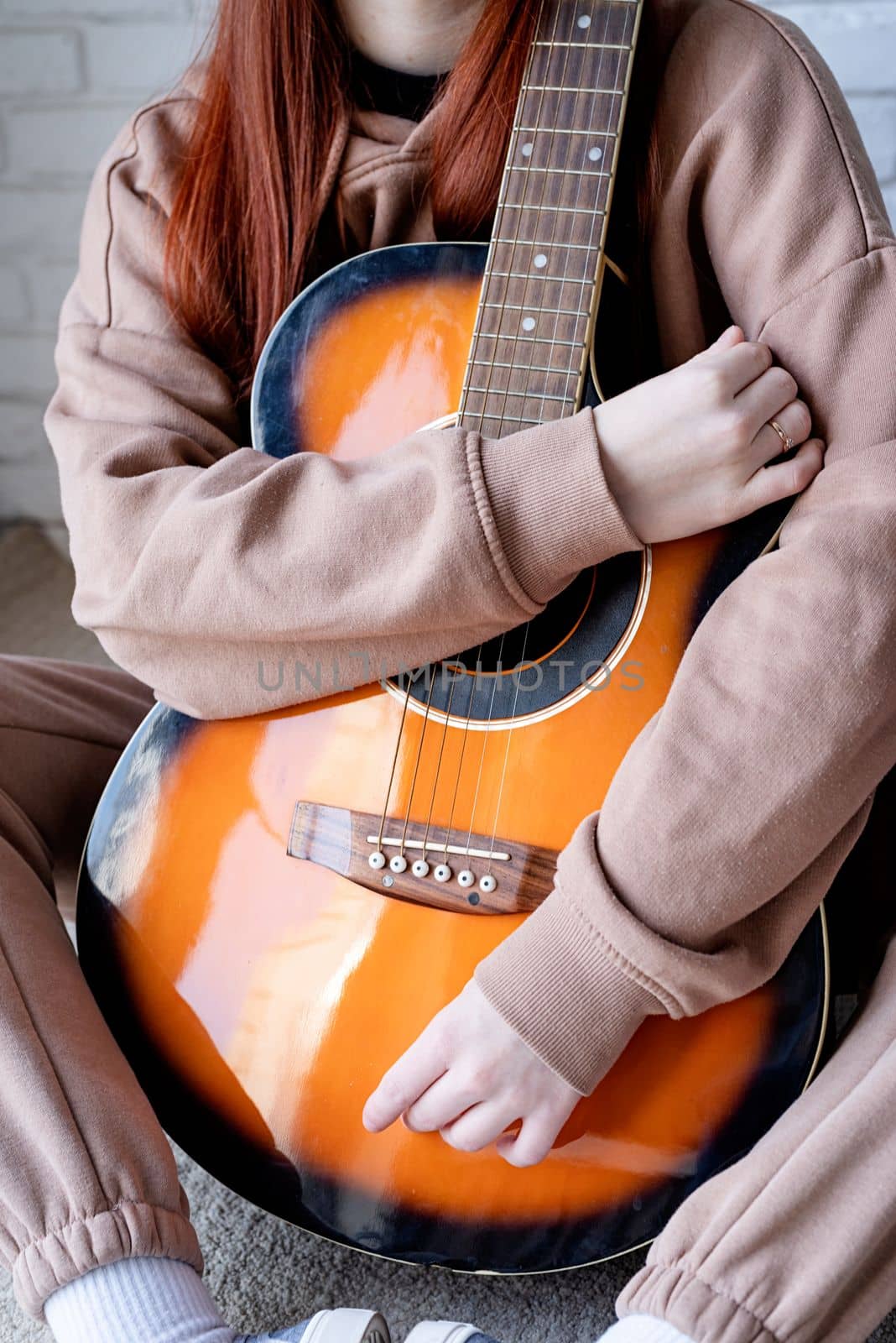 young caucasian red-haired woman sitting on rug and playing acoustic guitar at home