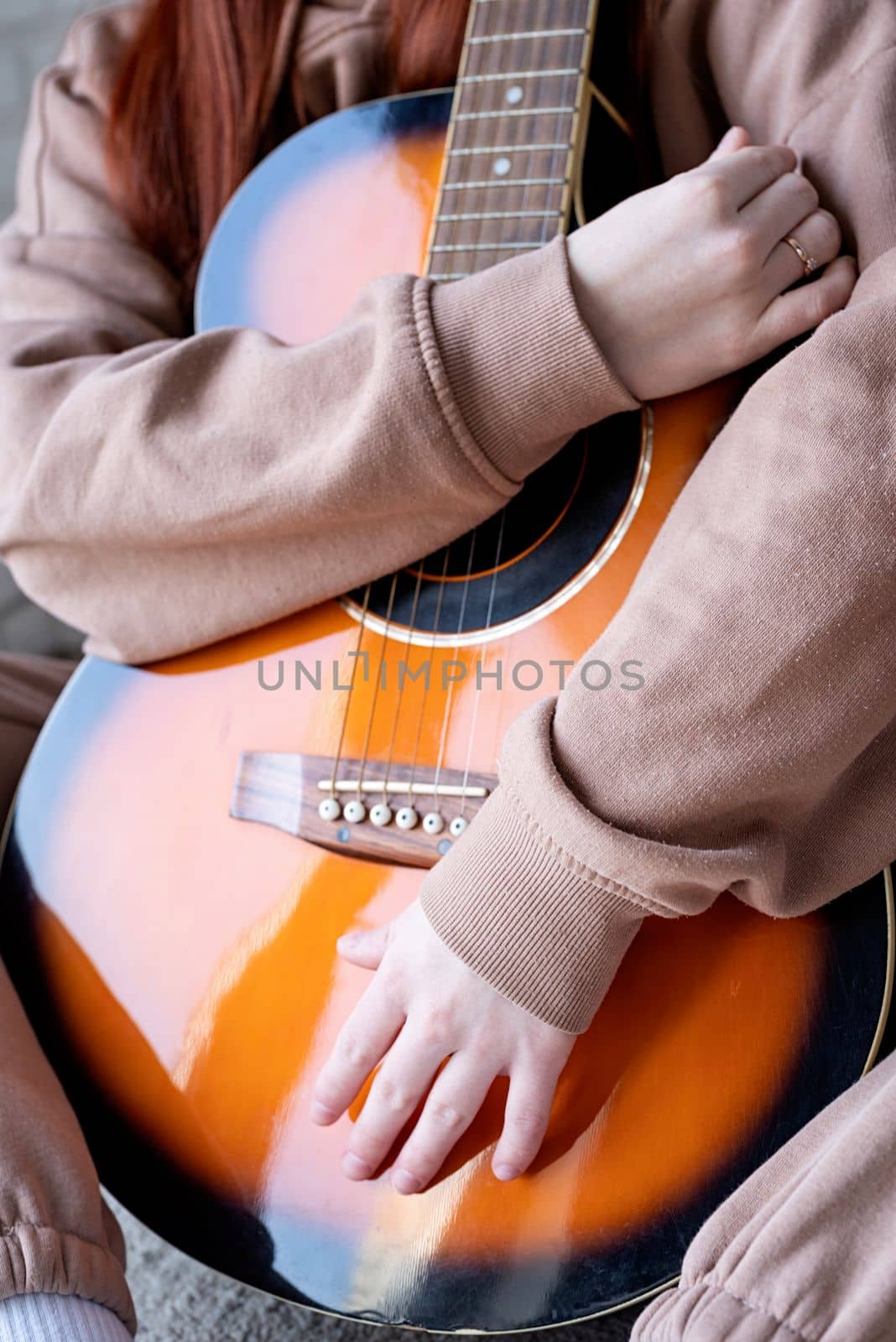 young caucasian red-haired woman sitting on rug and playing acoustic guitar at home