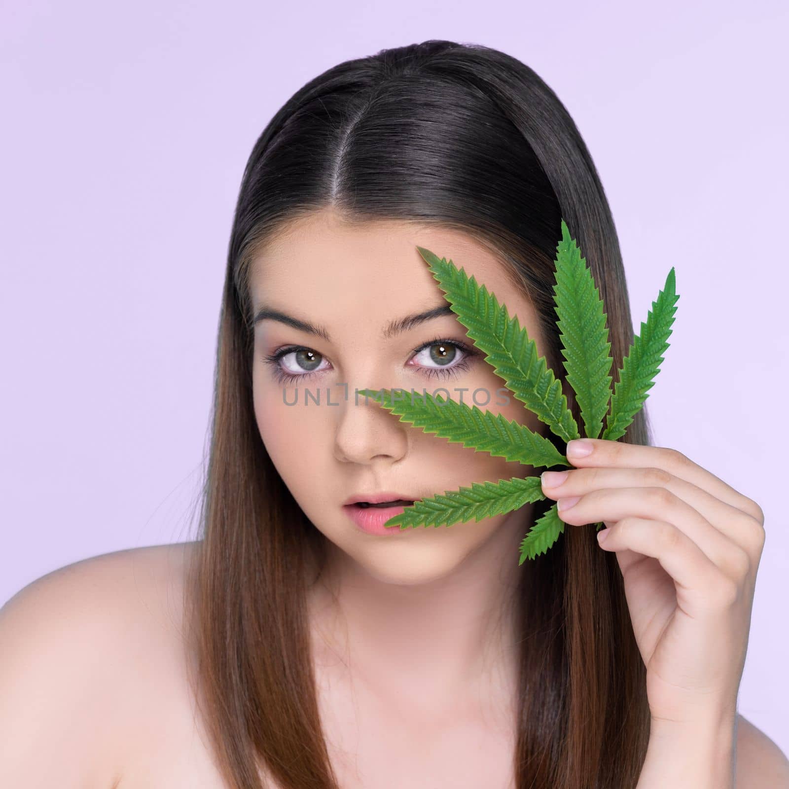 Closeup portrait of charming girl with fresh skin holding green leaf for beauty skin care made from cannabis leaf. Cosmetology and cannabis concept with isolated background.