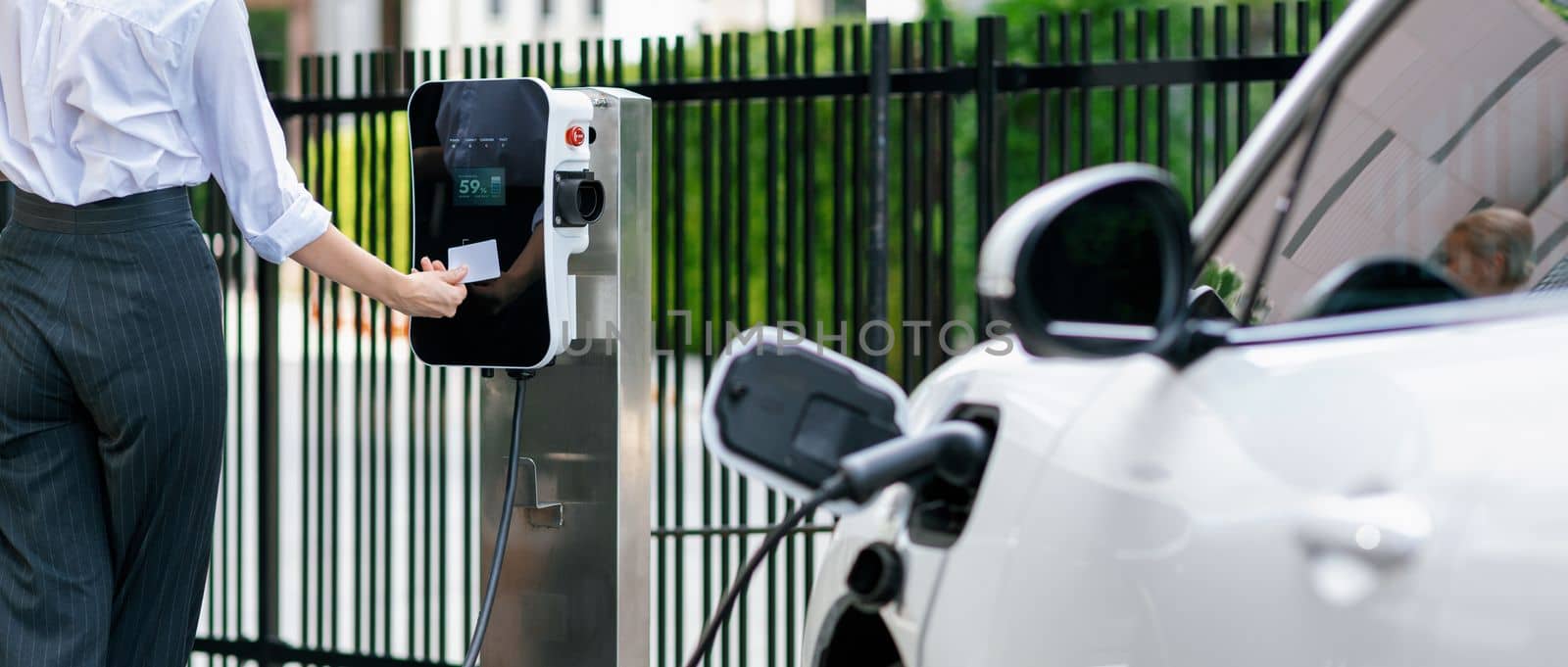 Progressive woman pay for charging point to power electric rechargeable vehicle. by biancoblue