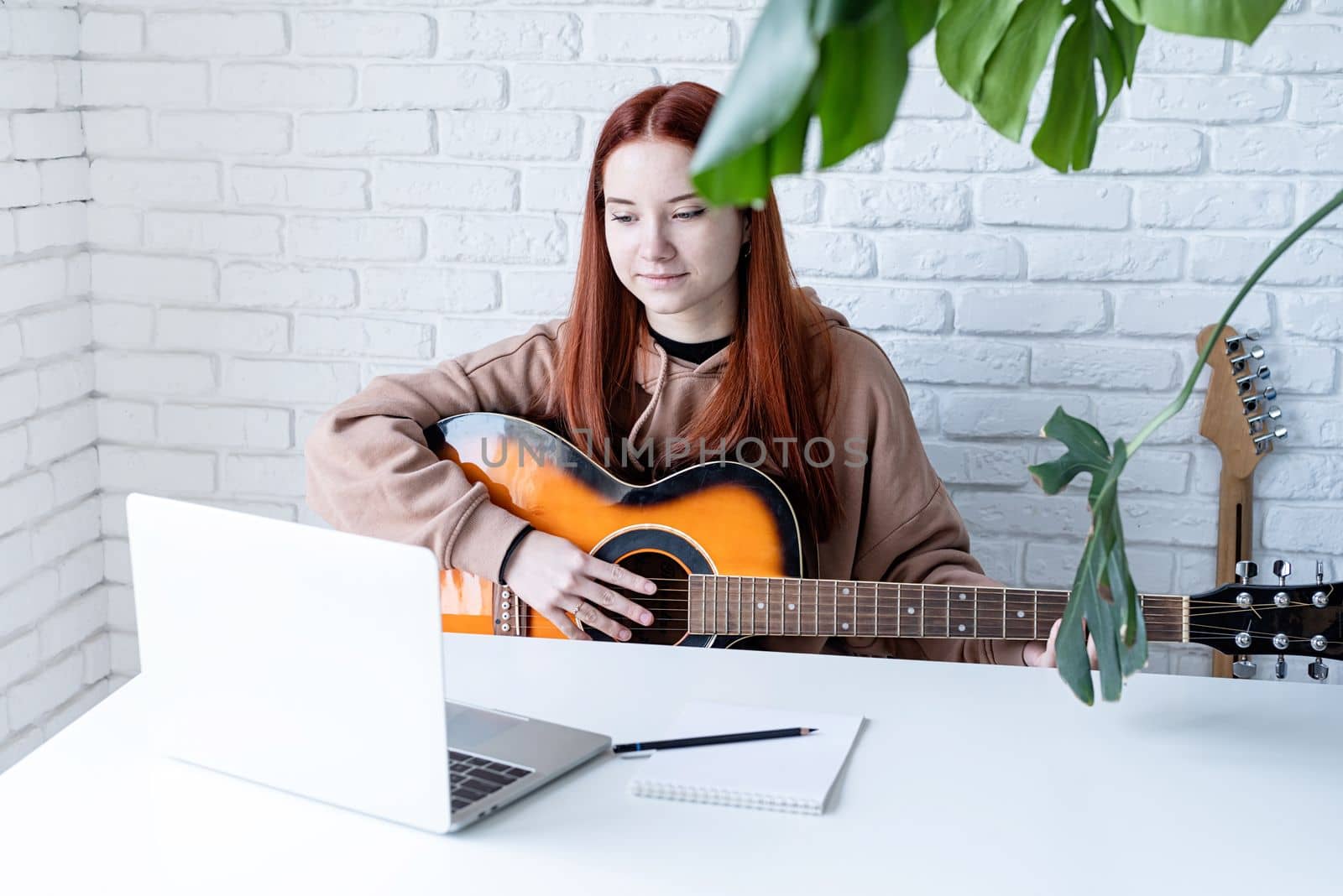 Young woman learning to play guitar at home by Desperada