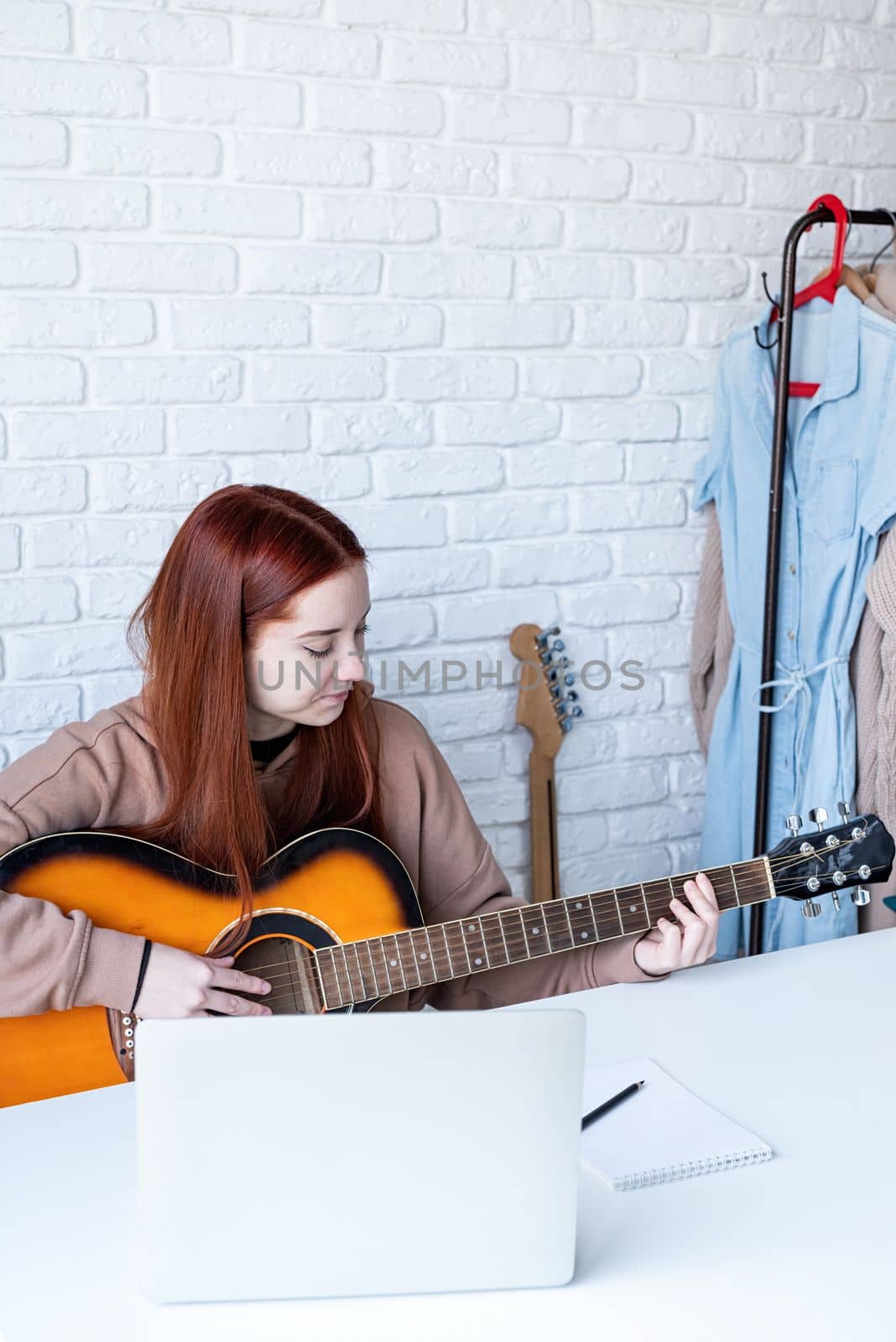 Young woman learning to play guitar at home by Desperada