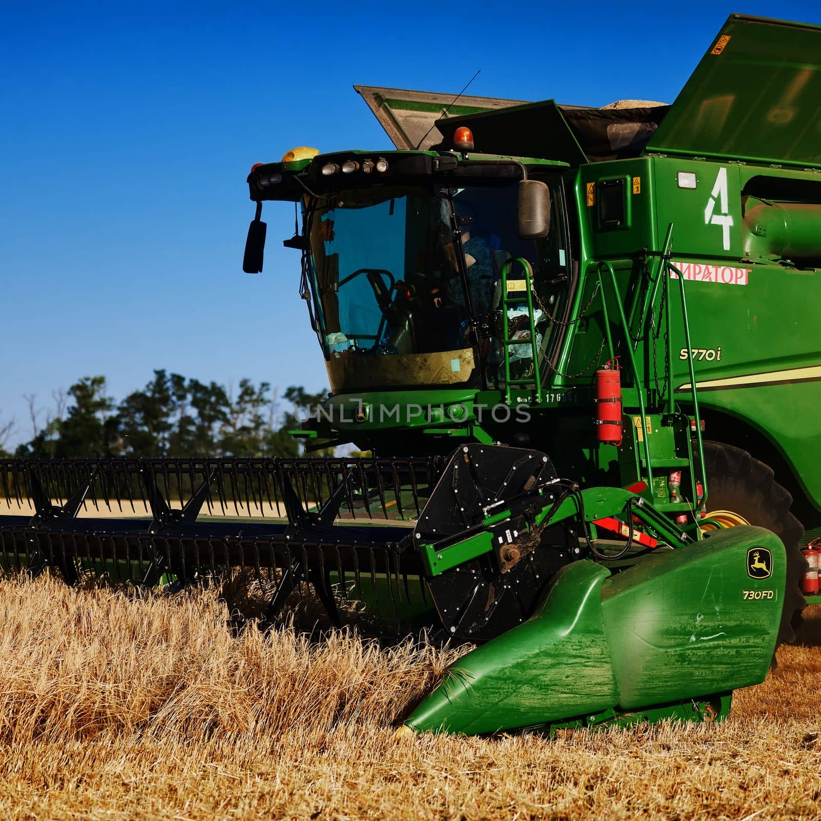 John Deere harvester works in the field. Combine Harvesting Wheat. Field field of cereals during harvesting. Modern equipment works. 07.07.22, Rostov region, Russia by EvgeniyQW