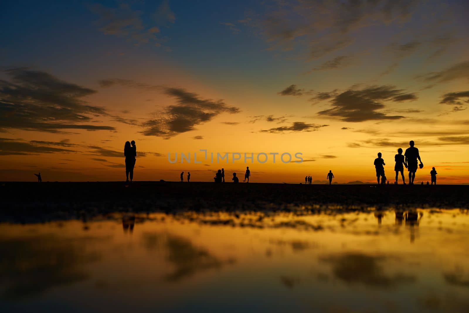 Silhouettes of people walking on the ocean floor after the evening tide. Incredible colors of the evening sky.