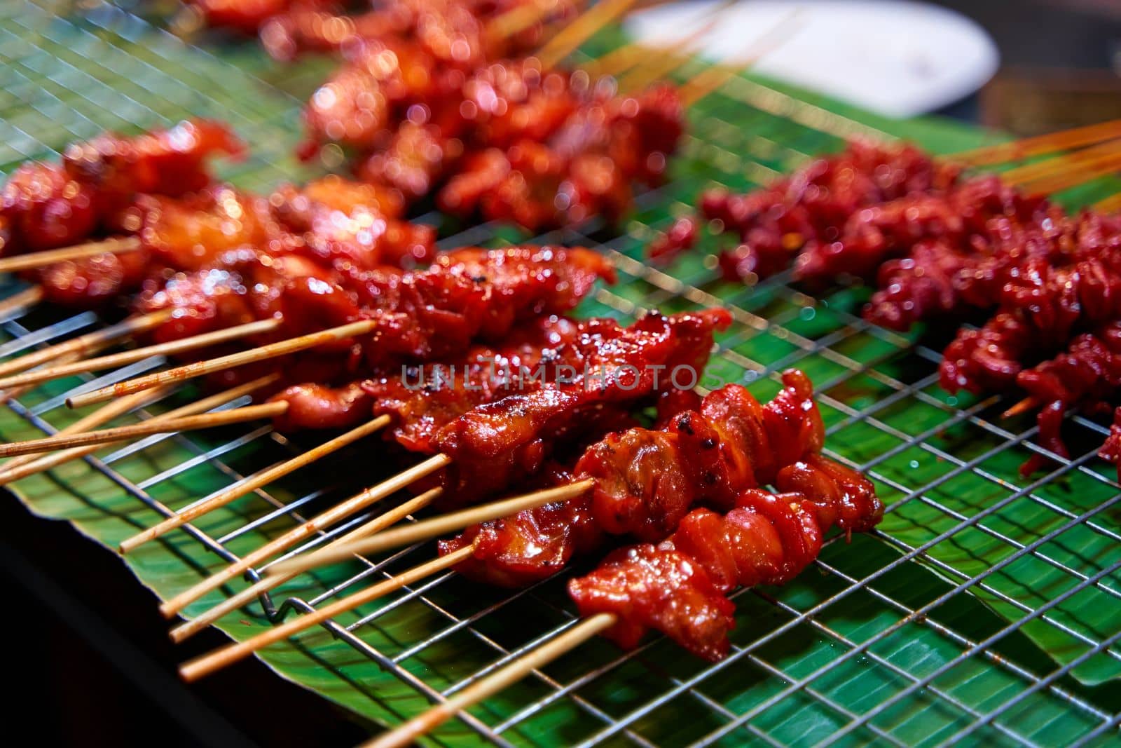 A close-up of a barbecued chicken fillet on a wooden stick. Asian sate.