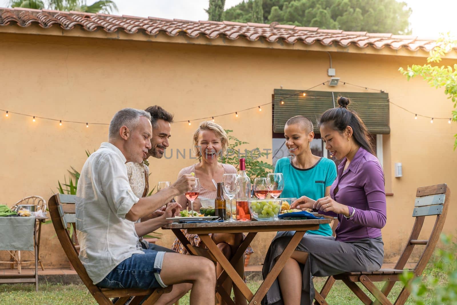 Happy middle-aged men and women eating healthy food at country house picnic. Lifestyle concept with cheerful friends having fun together in afternoon relaxation time.