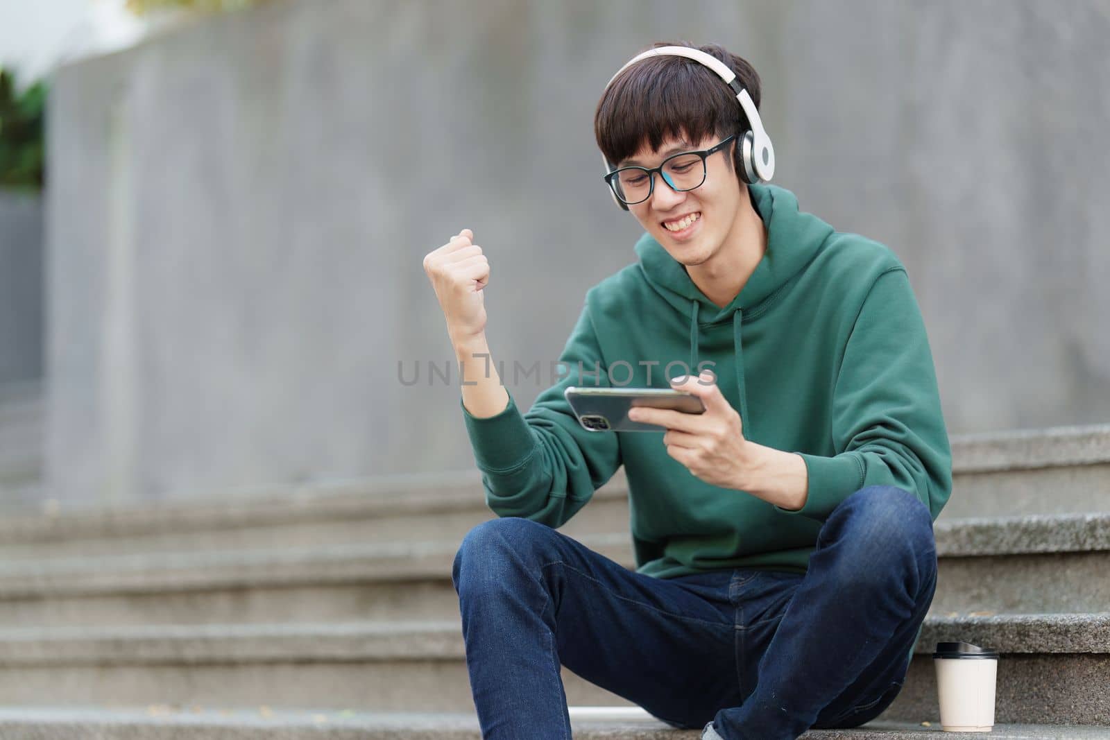 Young Asian student using phone and celebrate while in victory position.