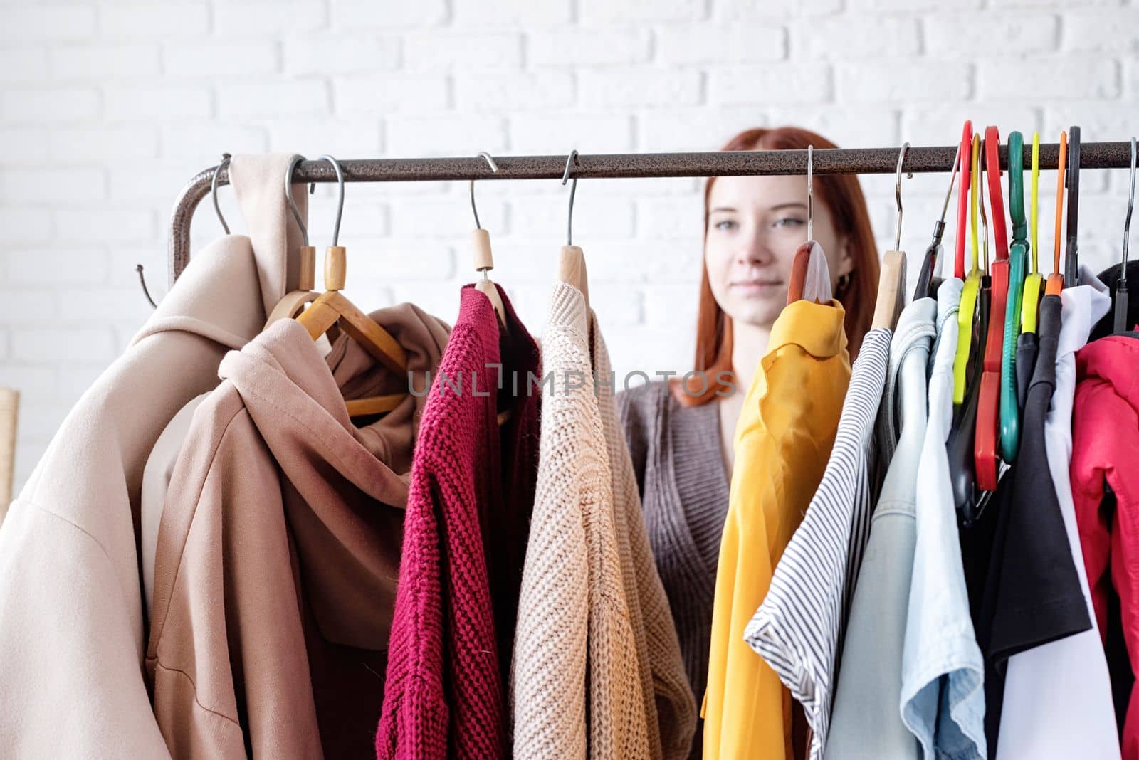 beautiful young woman in trendy outfit standing in front of hanger rack and choosing outfit dressing. Selection of a wardrobe, stylist, shopping. Clothes designing