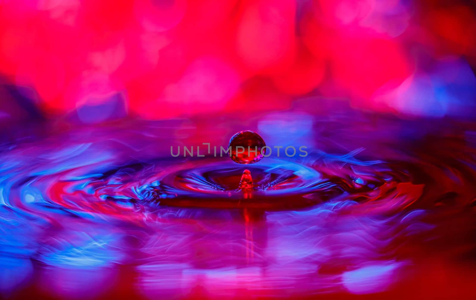 A transparent drop with a red-violet background falls into the water. Abstract colorful background. by Yurich32