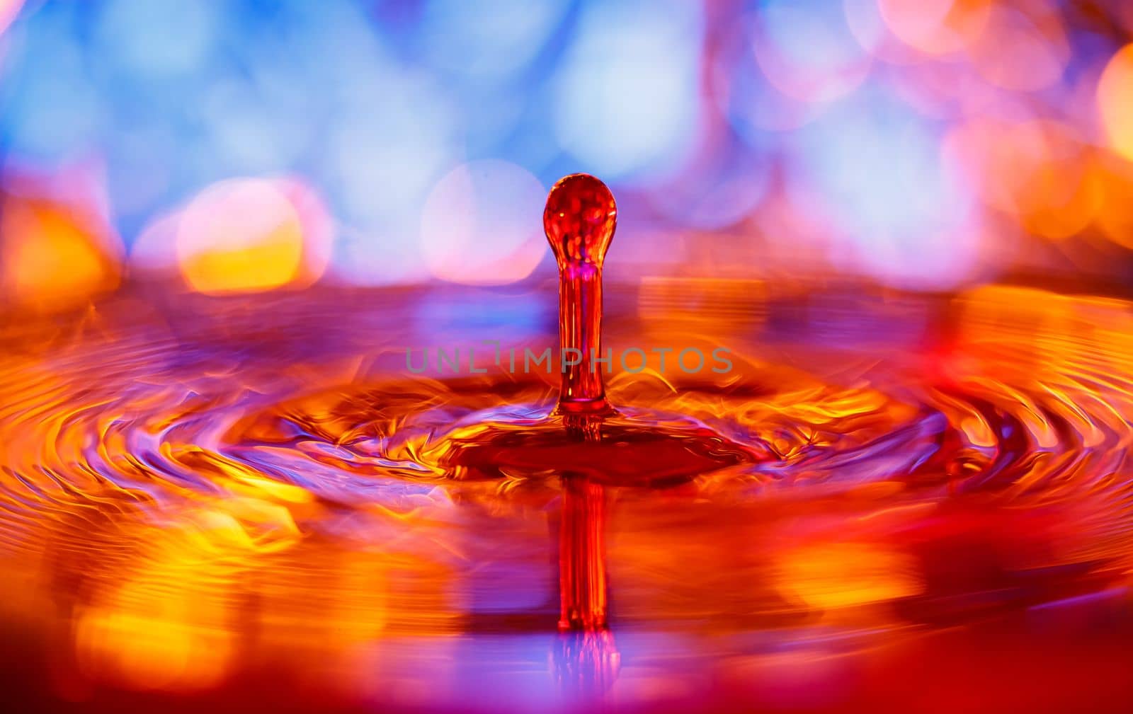 A transparent drop with a red-yellow background falls into the water. Abstract colorful background. by Yurich32