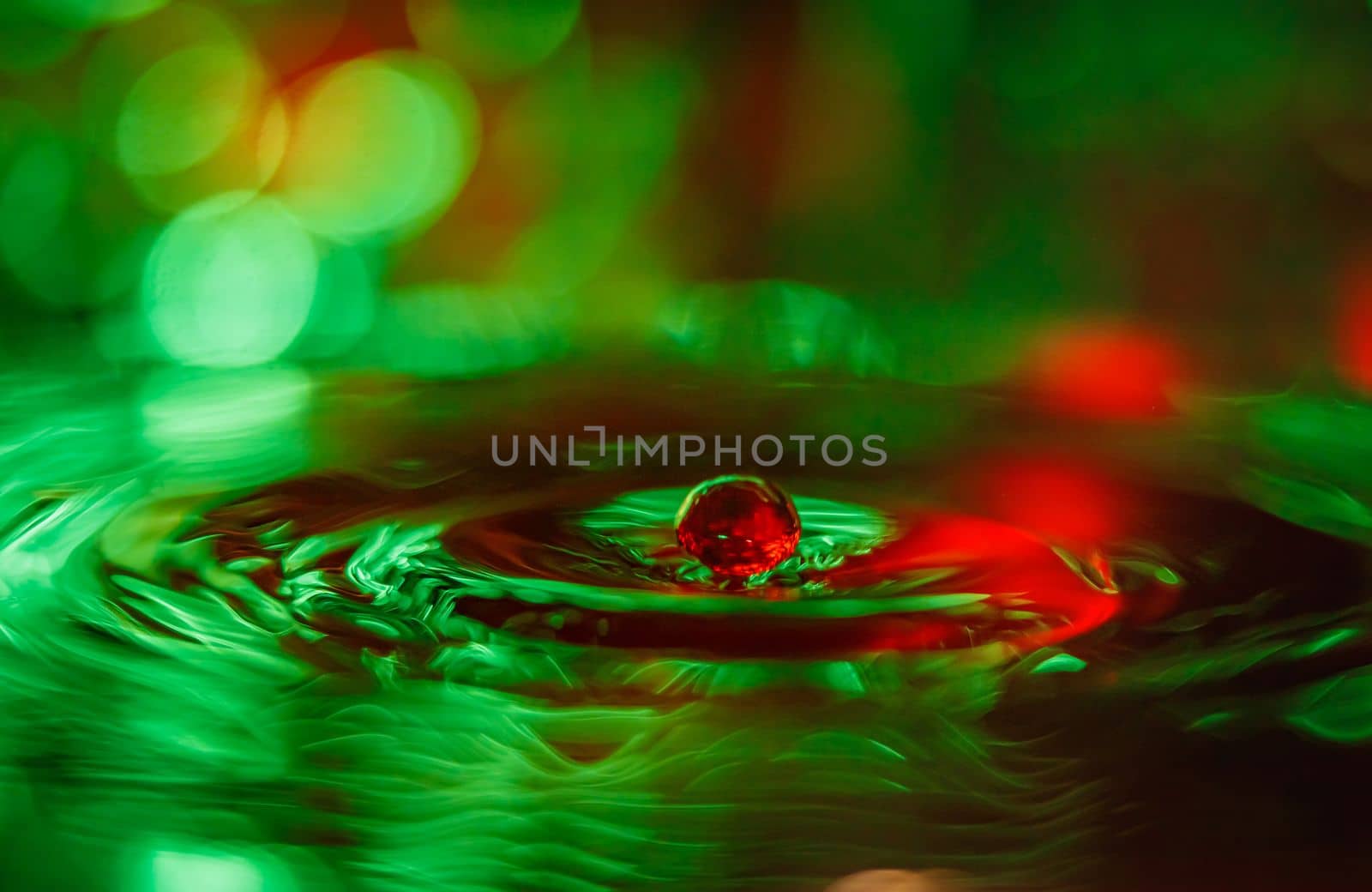 A transparent drop with a green background falls into the water. Abstract colorful background