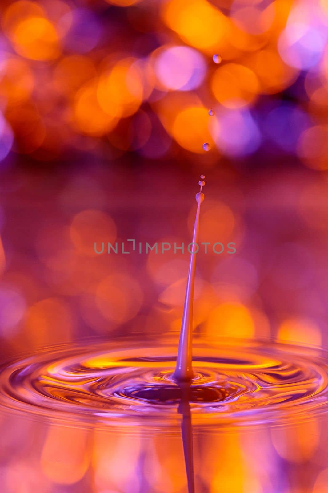 The drop falls into a dense liquid with an orange background. Abstract colorful background