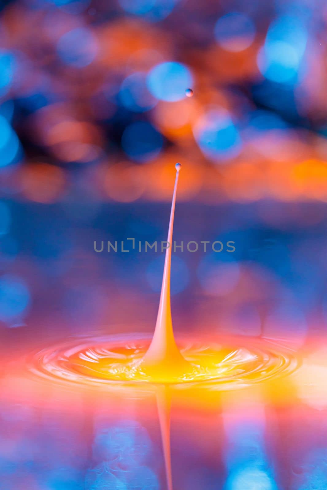 The drop falls into a dense liquid with a blue-yellow background. Abstract colorful background