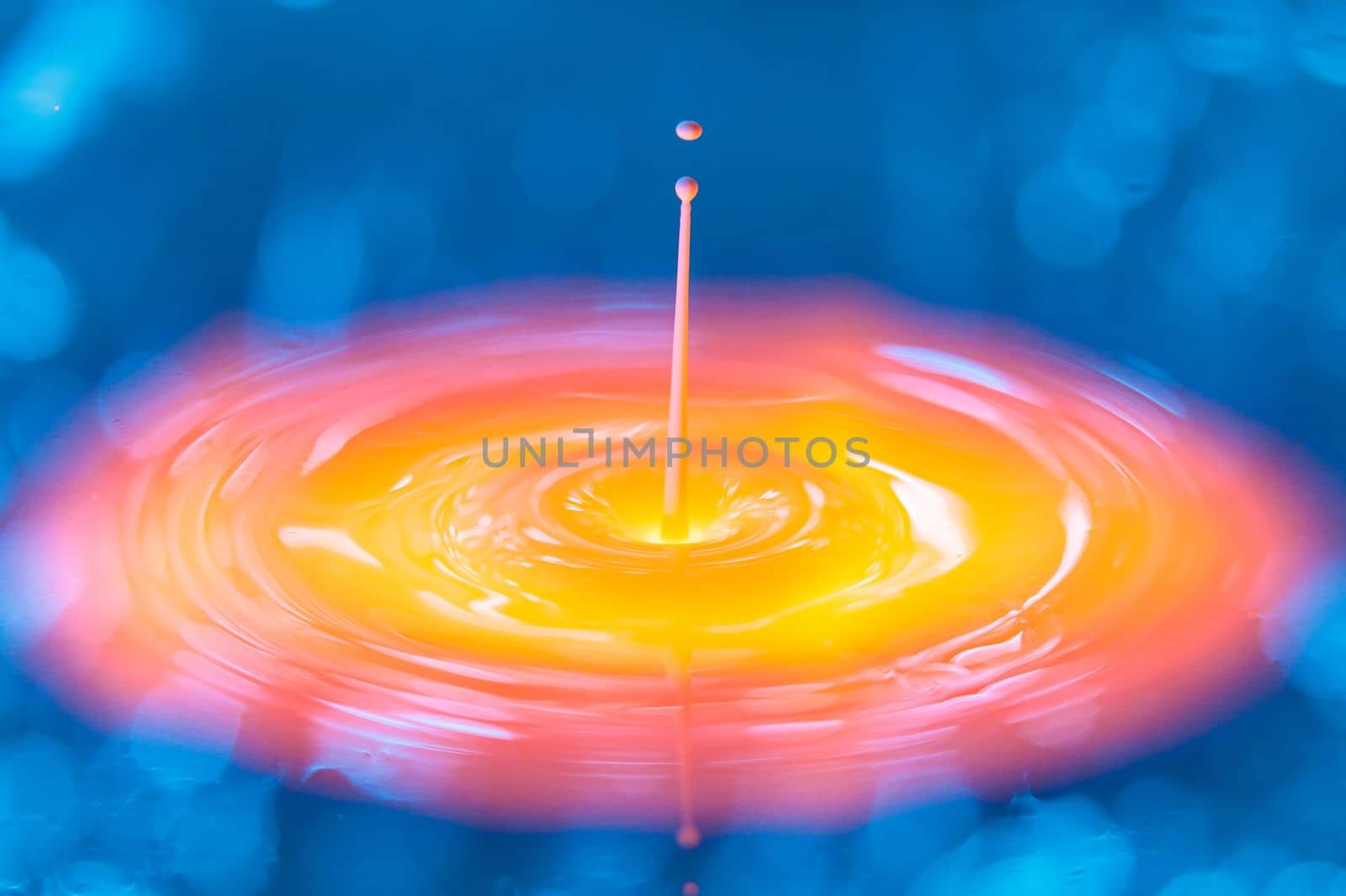 The drop falls into a dense liquid with a blue-yellow background. Abstract colorful background