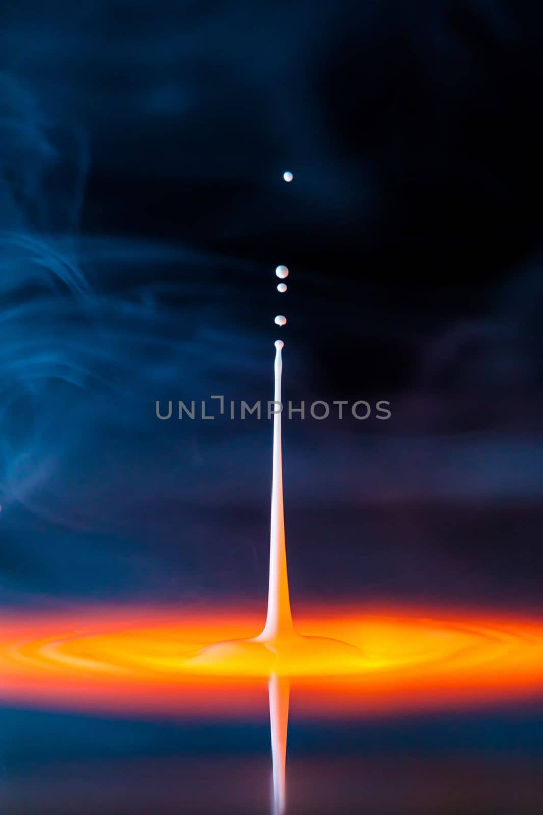 The drop falls into a thick liquid with a blue-yellow background in the smoke. Abstract colorful background