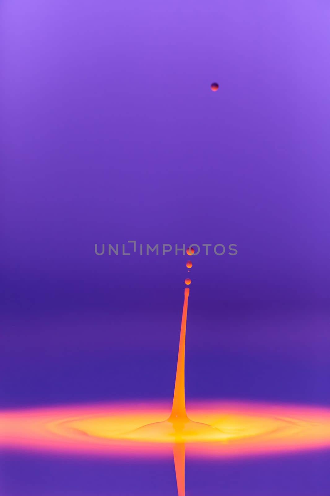 A drop falls into a thick liquid with a violet-yellow background. Abstract colorful background