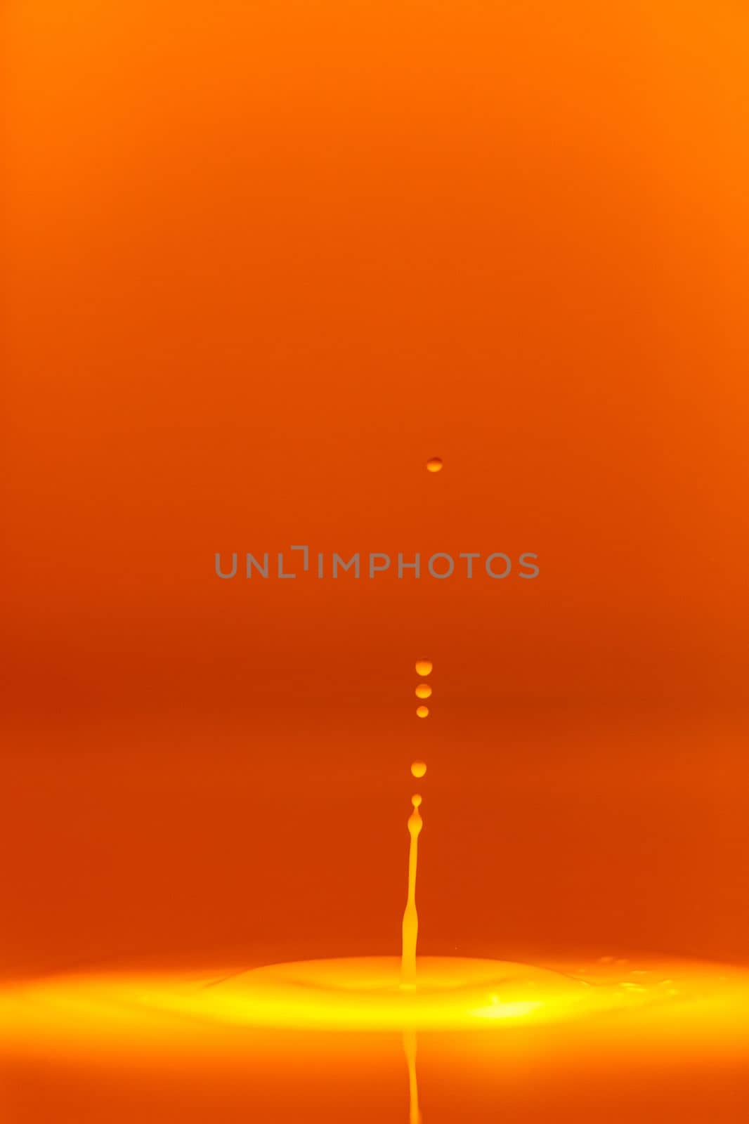 The drop falls into a dense liquid with an orange background. Abstract colorful background