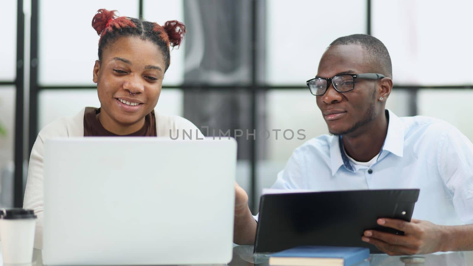 colleagues sitting together at a table in a modern office talking and using a laptop