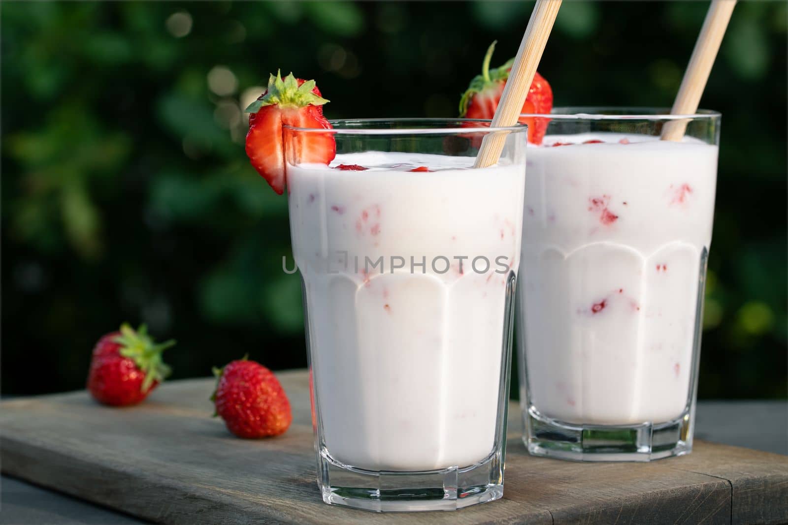 Strawberry smoothie in two glass glasses and fresh strawberries on a wooden table in the yard.