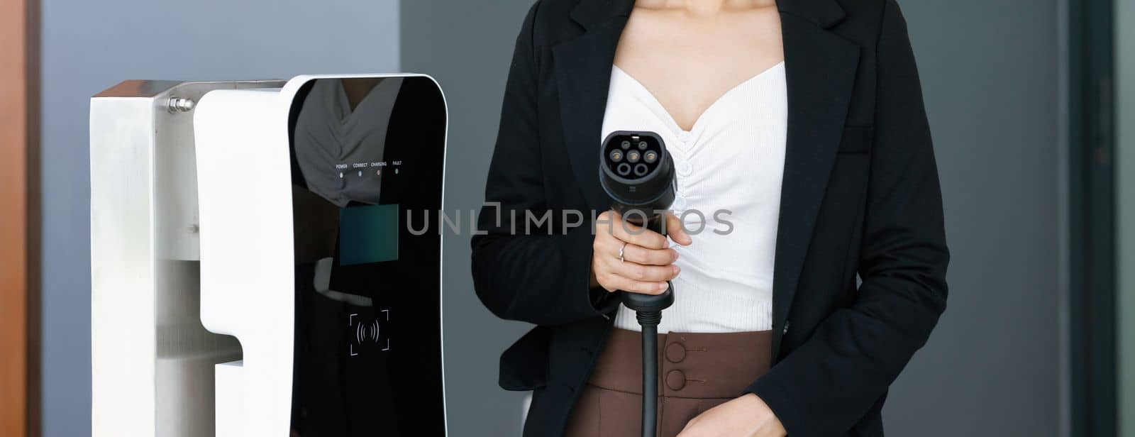 Closeup asian woman holding and pointing an EV plug, a home charging station providing a sustainable power source for electric vehicles. Alternative energy for progressive lifestyle.