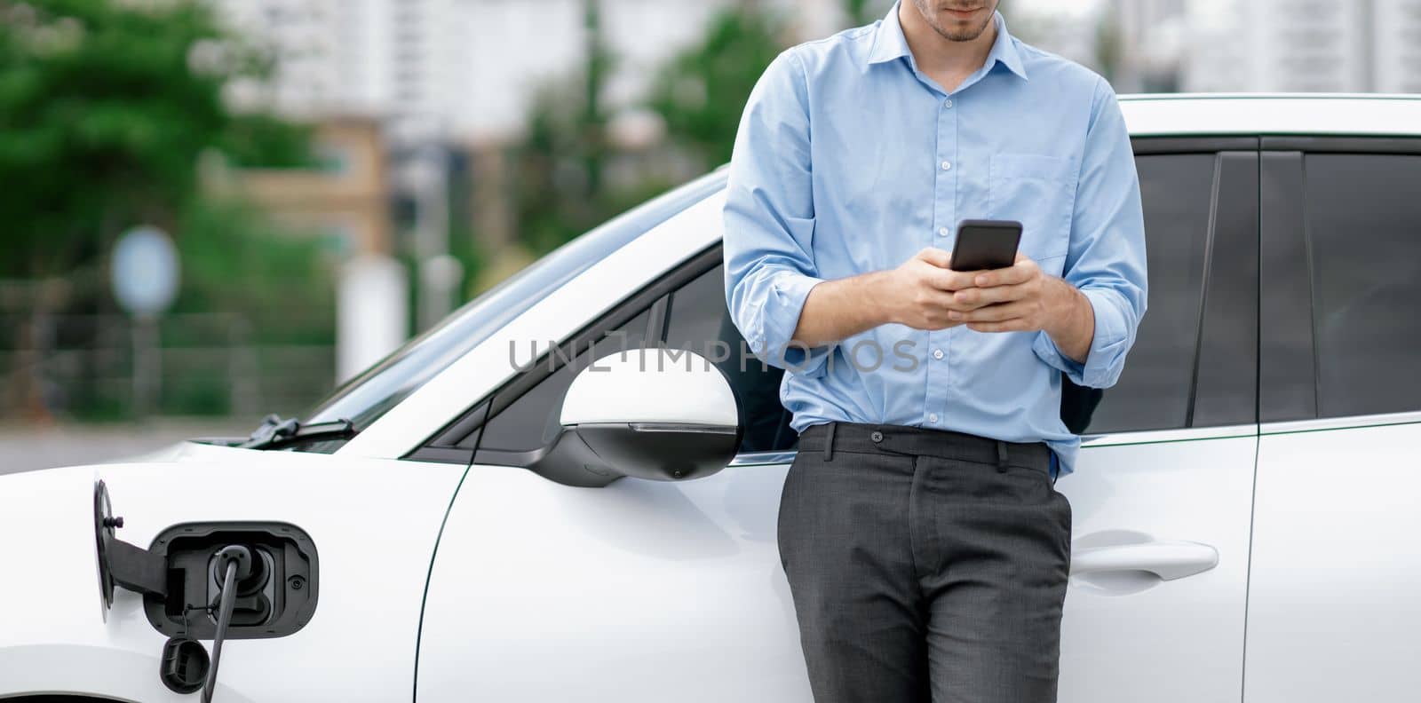 Progressive businessman talking on the phone with recharging electric vehicle. by biancoblue