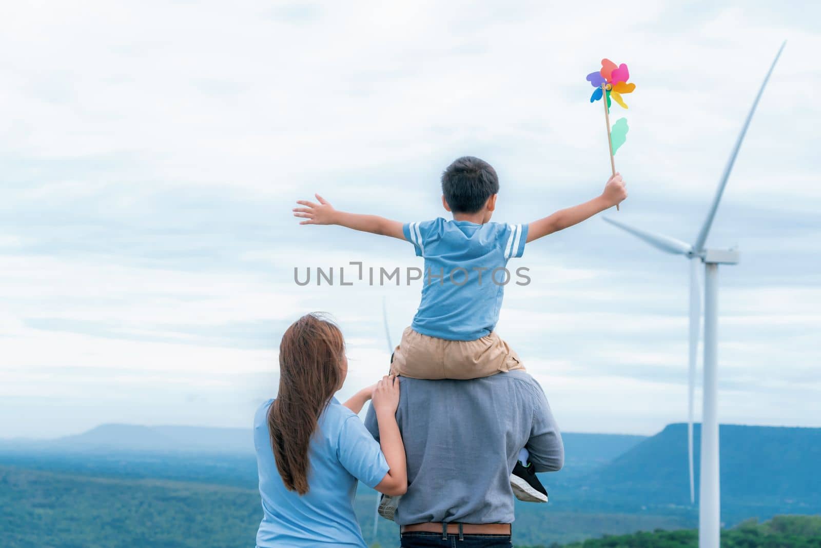 Progressive happy family enjoying their time at wind farm for green energy production concept. Wind turbine generators provide clean renewable energy for eco-friendly purposes.