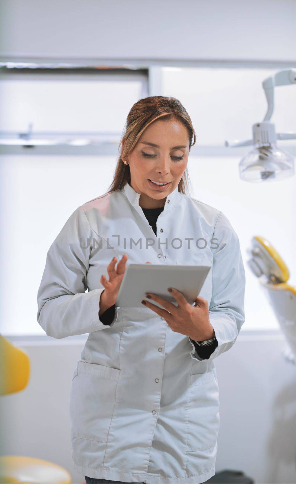 Your appointment is with me today. a cheerful young female dentist working on her laptop while standing in her office. by YuriArcurs