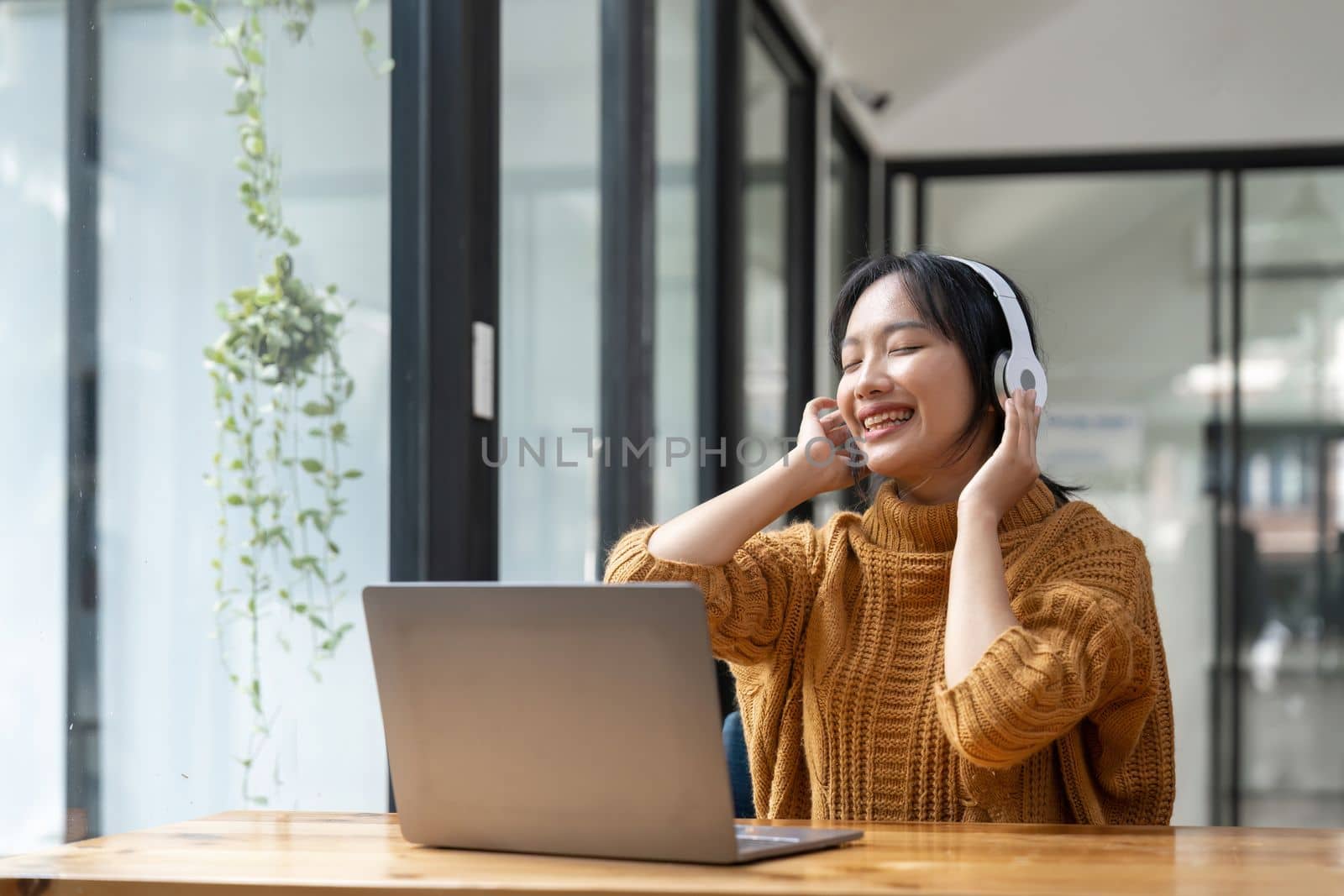 Overjoyed millennial girl wearing headphones have fun moving listening to music relax on laptop by nateemee