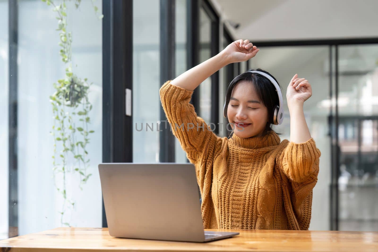 Overjoyed millennial girl wearing headphones have fun moving listening to music relax on laptop.