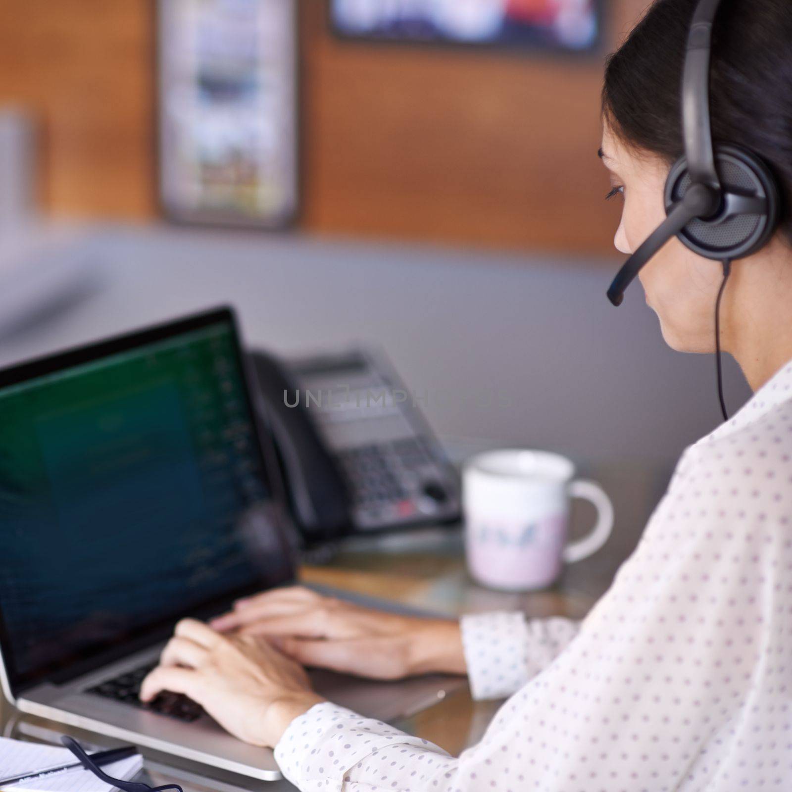 Taking your call. an attractive young businesswoman working on a laptop while wearing a headset