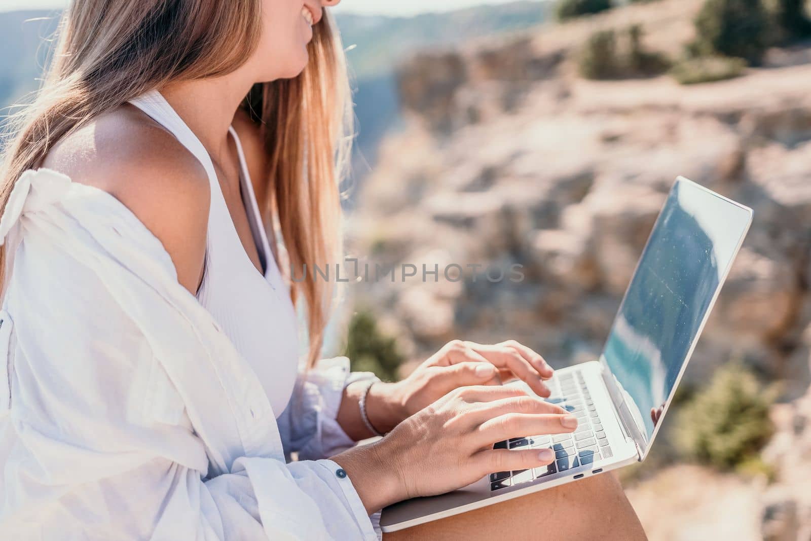 Digital nomad, Business woman working on laptop by the sea. Pretty lady typing on computer by the sea at sunset, makes a business transaction online from a distance. Freelance remote work on vacation