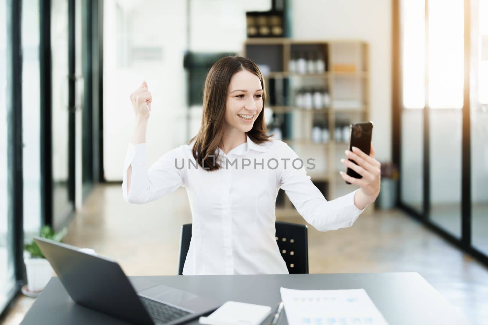Excited businesswoman using mobile phone while in office. by Manastrong