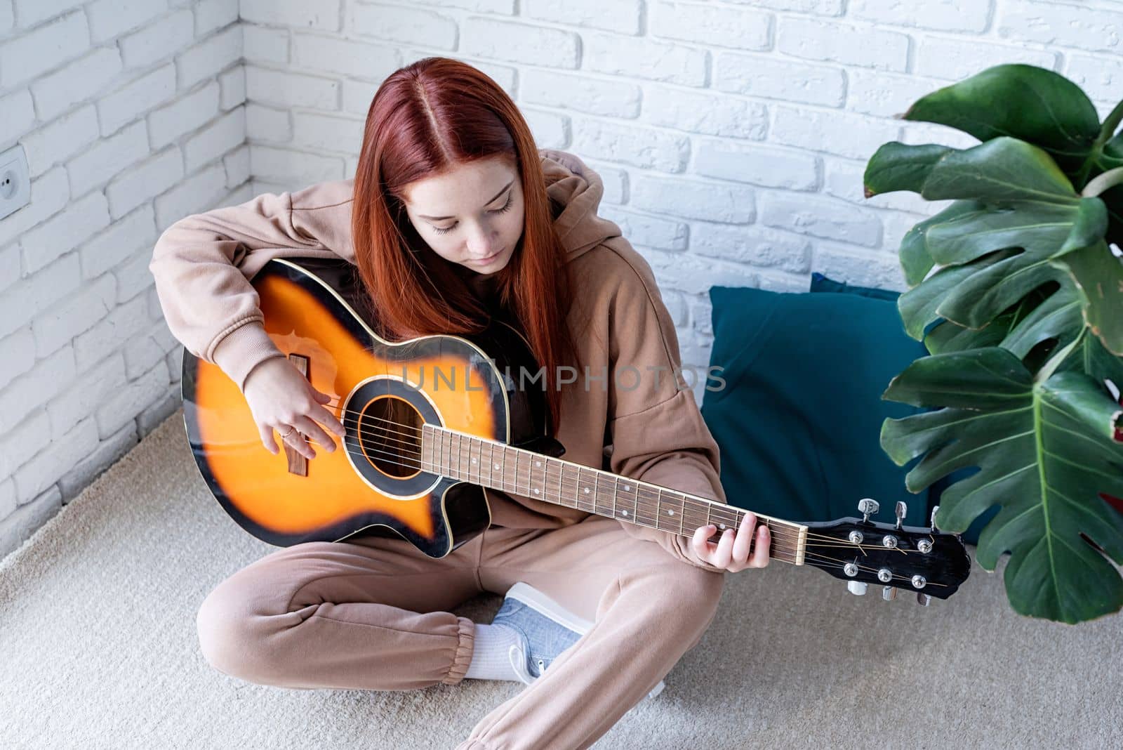 Young woman playing guitar at home by Desperada