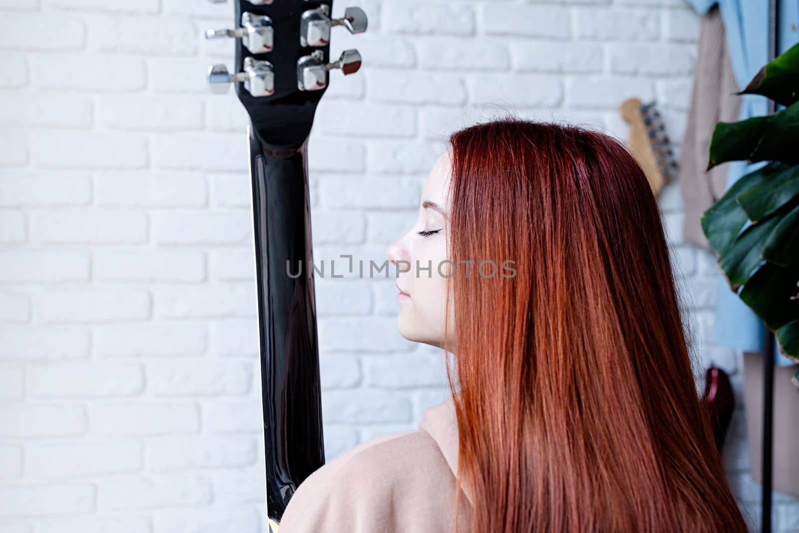 young caucasian red-haired woman sitting on rug and playing acoustic guitar at home