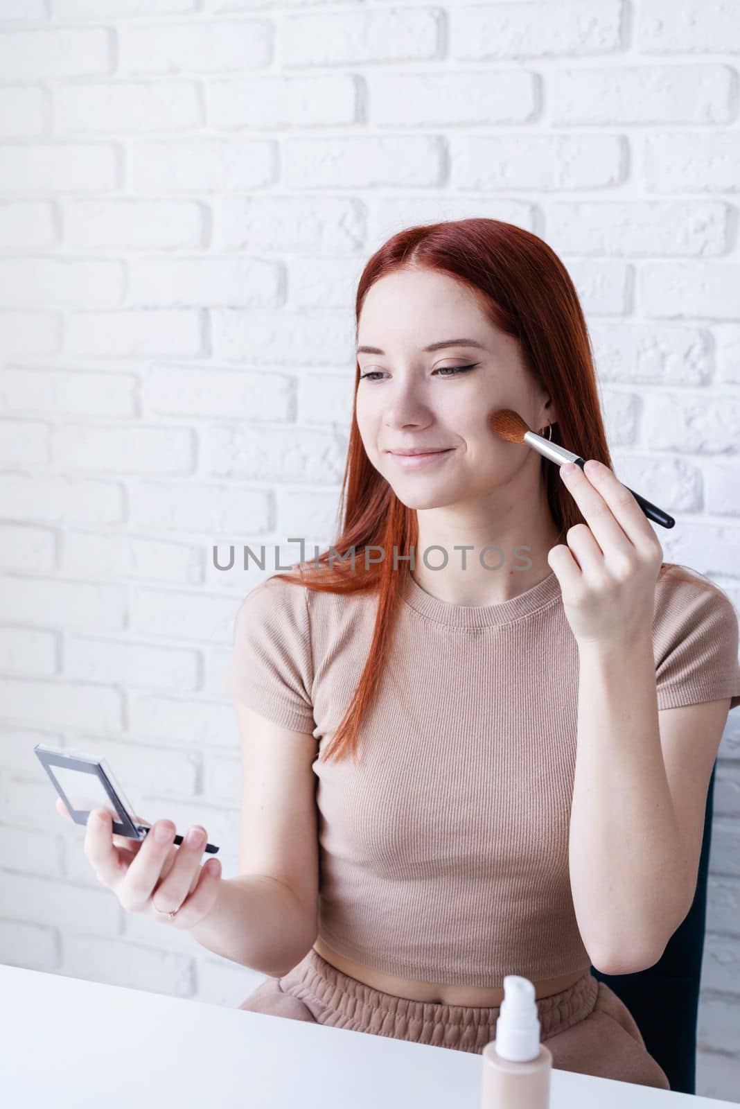 young beautiful woman holding make-up brushes and making up with cosmetics set at home