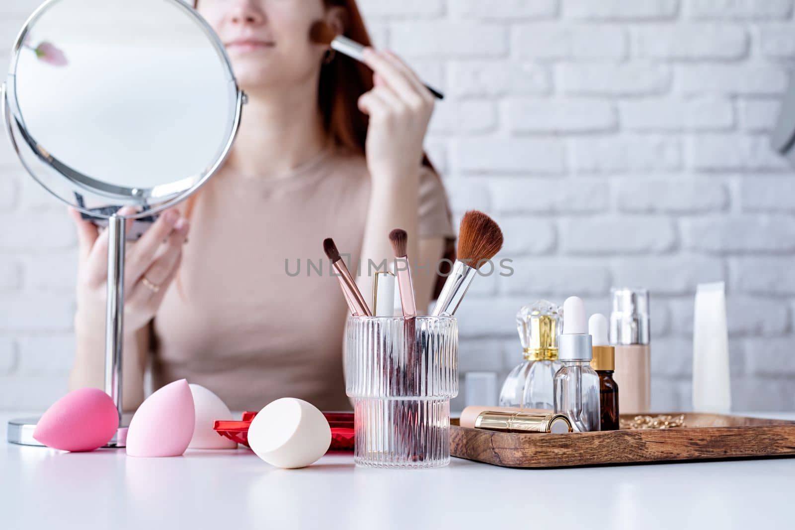 young beautiful woman holding make-up brushes and making up with cosmetics set at home