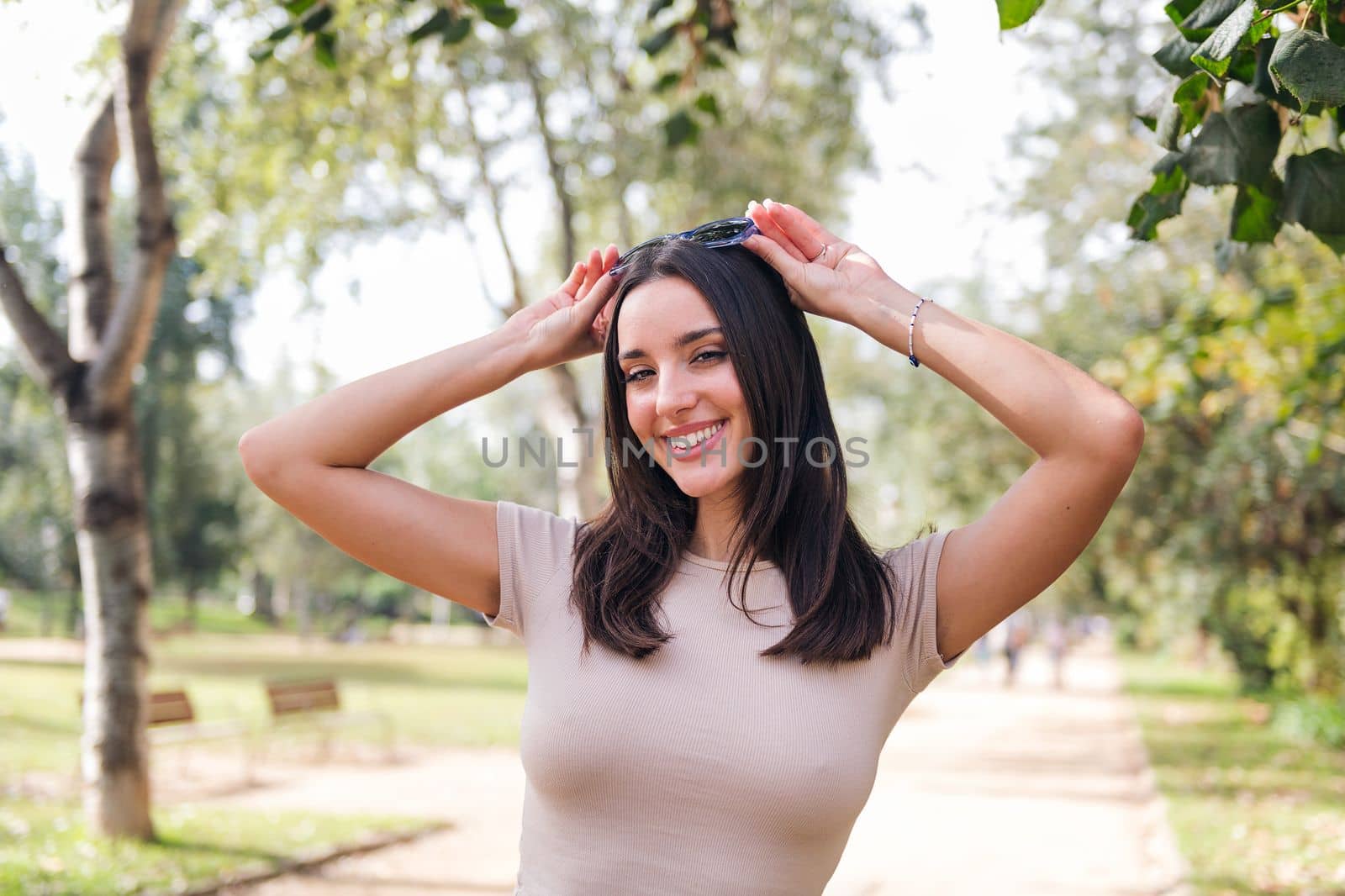 portrait of a cheerful caucasian woman putting on her sunglasses on her head smiling in the park, concept of youth and beauty