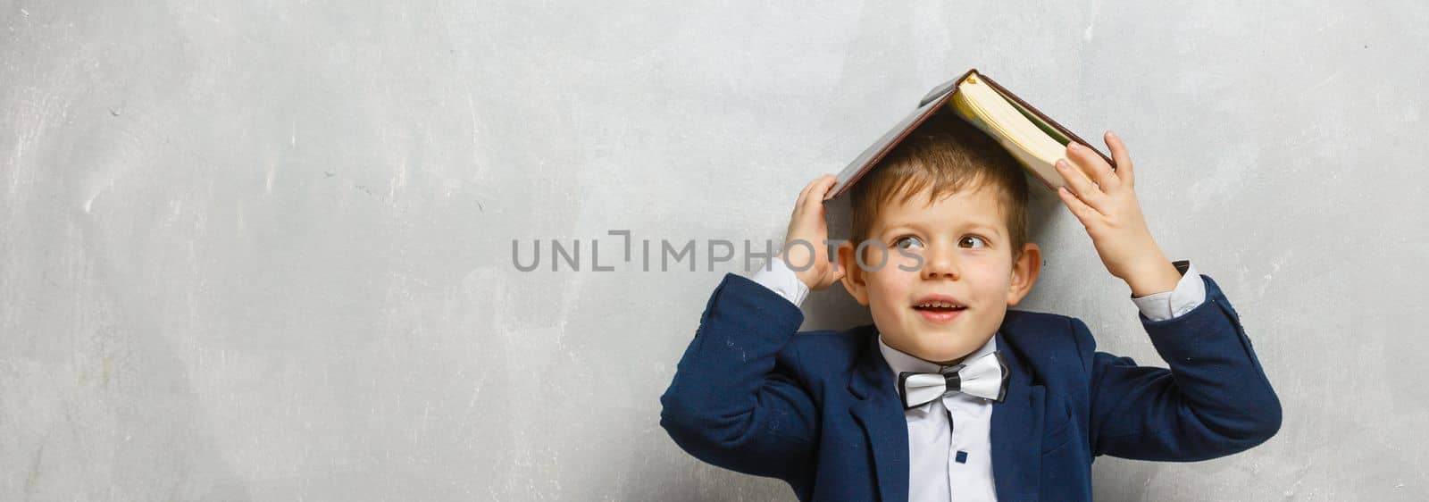 Sitting little schoolboy on gray background with space for text.