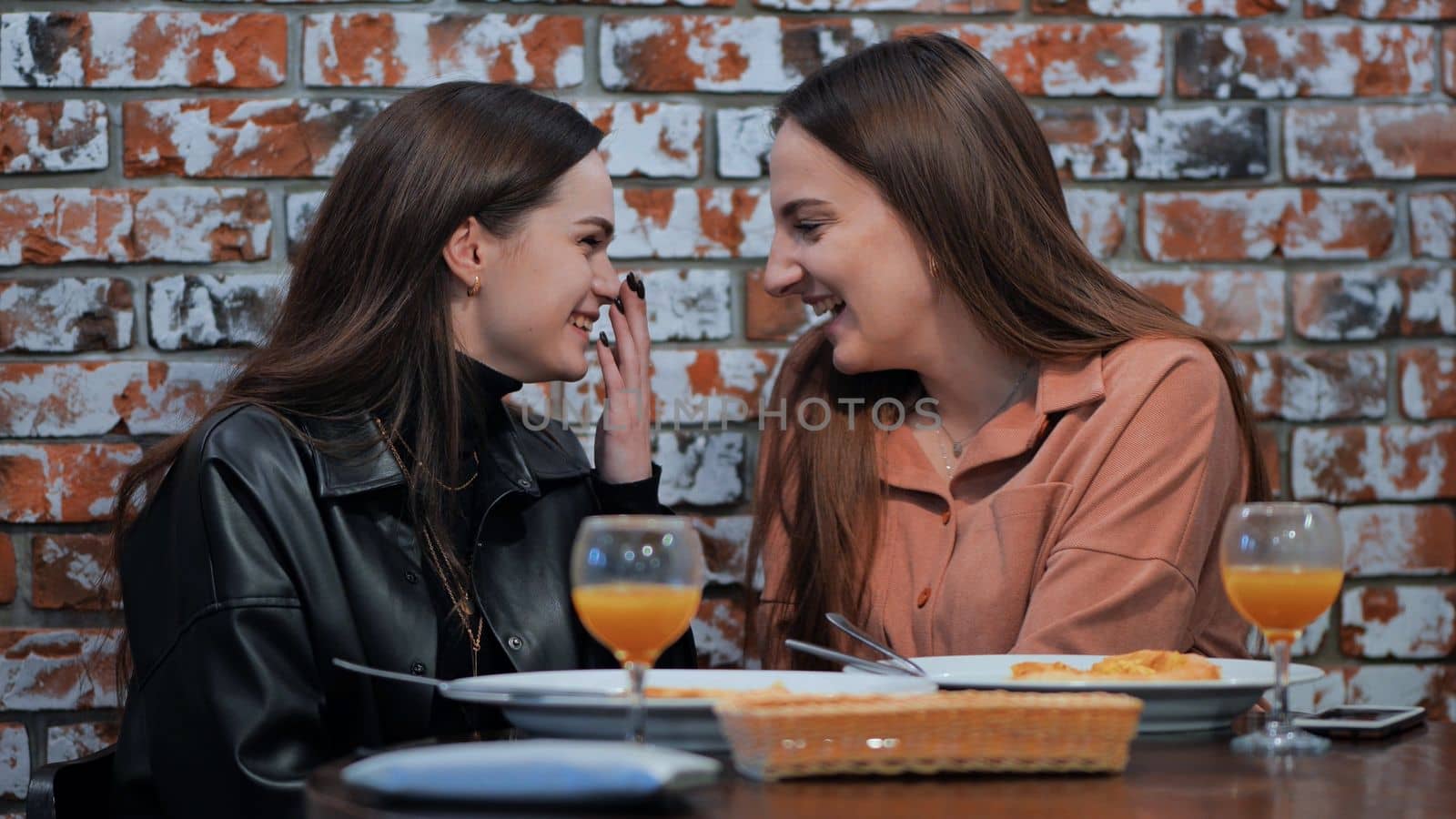 Young and cheerful girls gossip and whisper to each other while sitting in a cafe