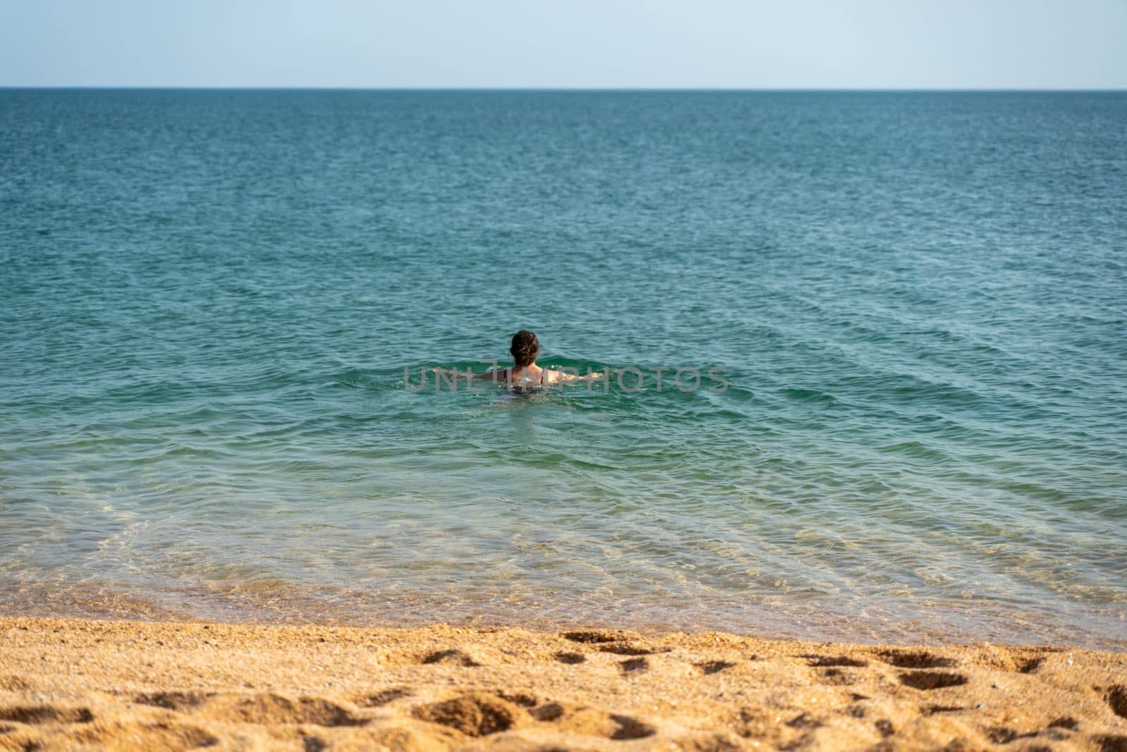 Woman sea swimsuit sand. The girl swims in the sea in a black swimsuit, the water is clean and transparent. Alone on the beach on a sunny day