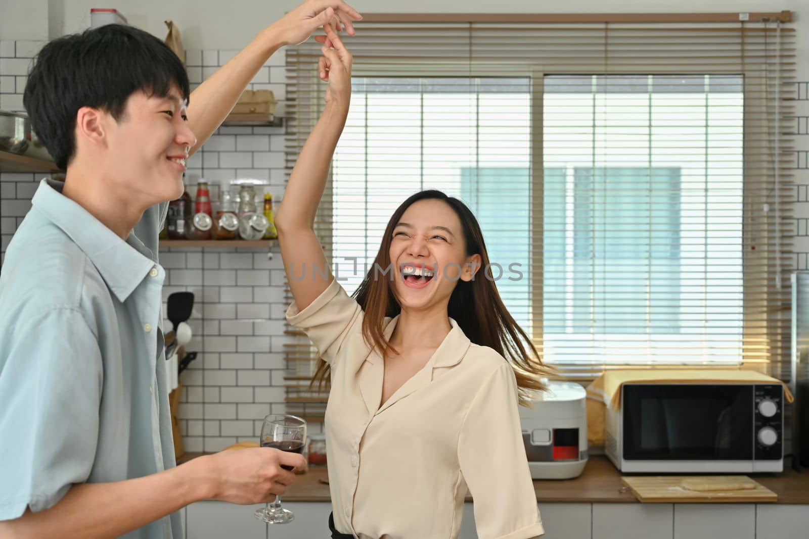 Overjoyed young couple dancing in kitchen, moving to favorite music while spending leisure weekend time together at home.