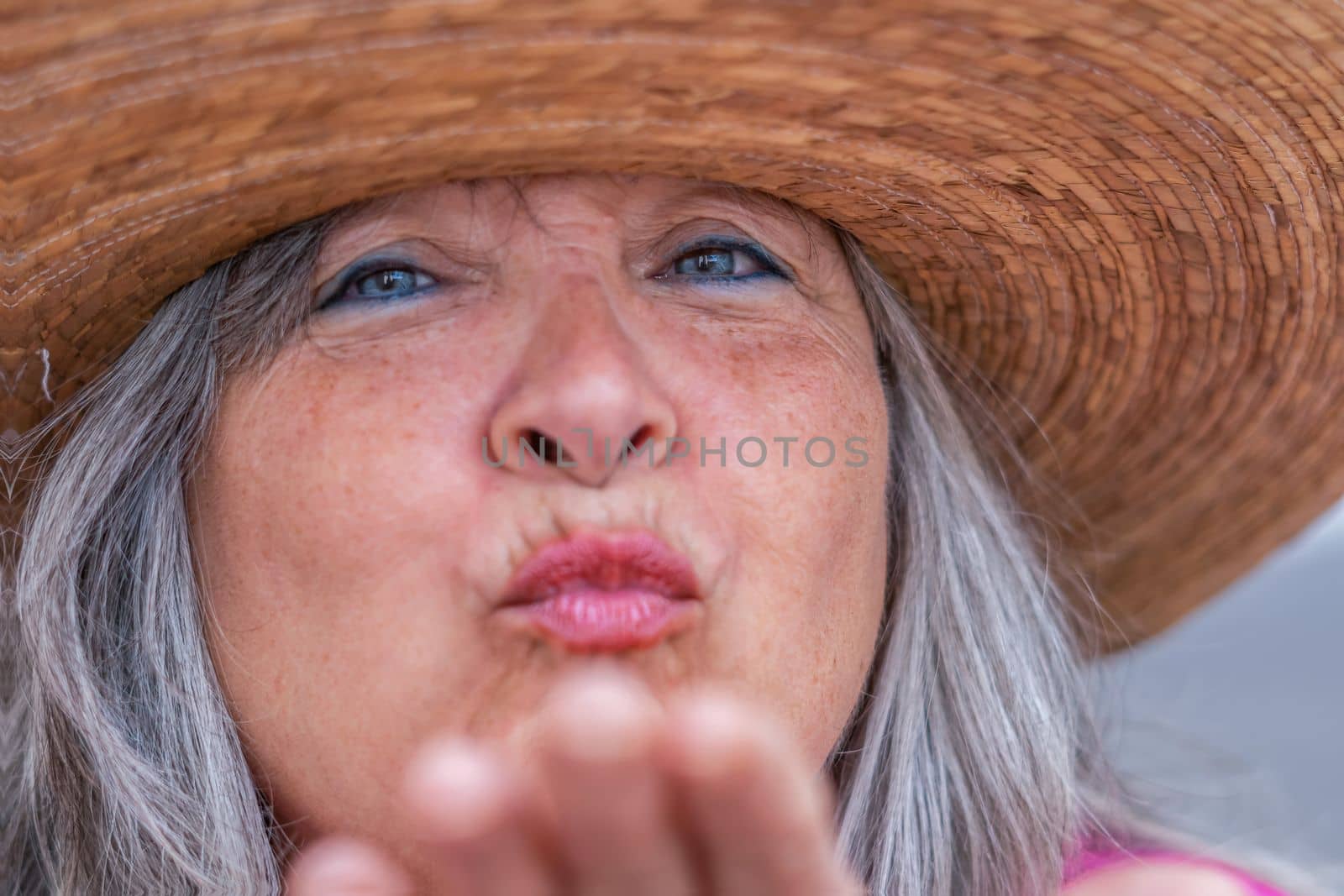 close-up of an older woman with a hat, white hair and blue eyes blowing a kiss with her hand