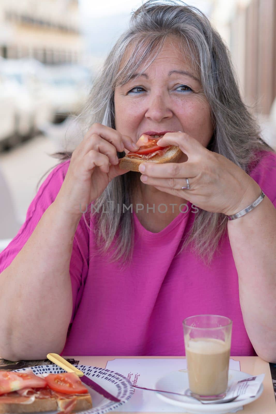 white-haired woman eating a ham and tomato toast and coffee by joseantona
